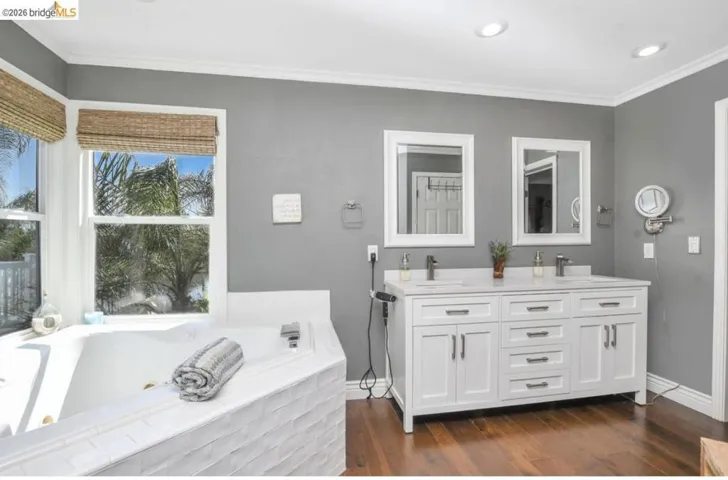 Bathroom featuring a corner soaking tub with white tile surround, dual pane windows, and wood-finish flooring