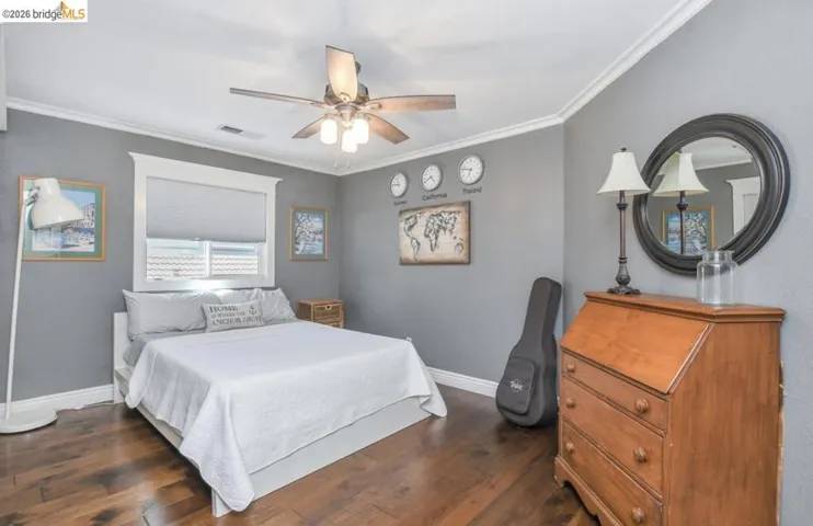 Bedroom featuring wood-finish flooring, a ceiling fan with integrated lighting, and a window with roller shade