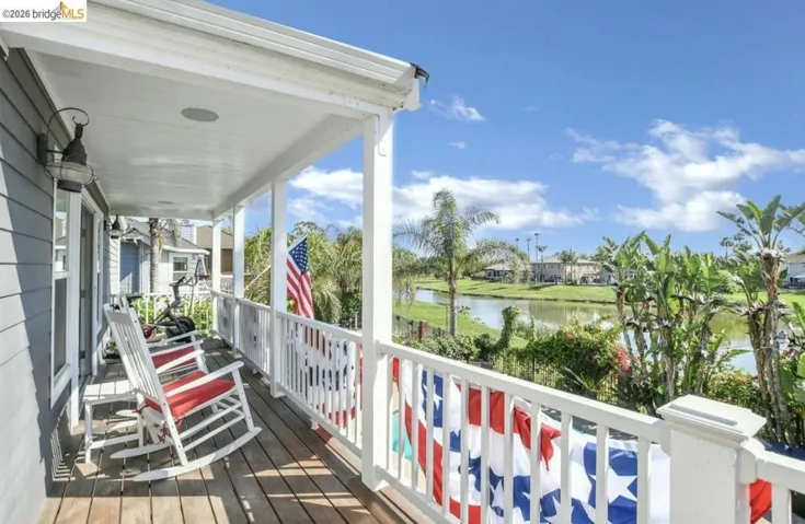 Covered outdoor balcony featuring wood-finish decking, white railing, and a shiplap exterior wall