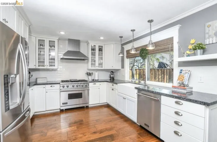 Gourmet kitchen featuring stainless steel appliances, white cabinetry, dark stone countertops, wood-finish flooring, and a farmhouse sink