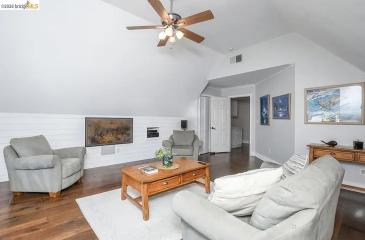 Spacious living area featuring sloped ceilings, wood-finish flooring, a ceiling fan with integrated lighting, and a horizontal shiplap accent wall with an integrated media niche