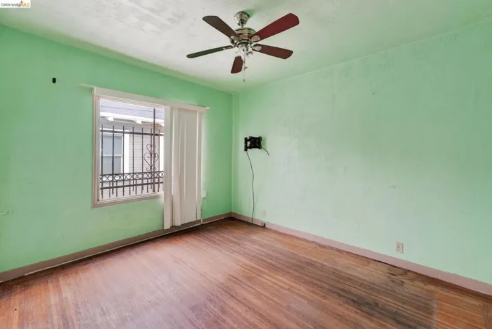 Room featuring wood-finish flooring, a ceiling fan, and a window with security bars