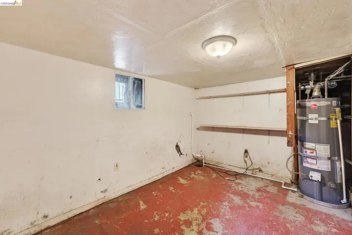 Utility room with red-toned concrete flooring, a water heater, and built-in shelving