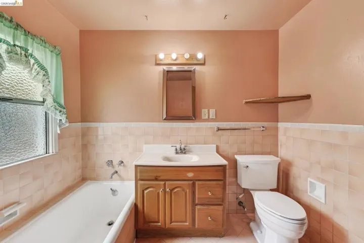 Bathroom featuring a white bathtub, a wood-finish vanity with a white countertop and integrated sink, a toilet, and textured privacy window