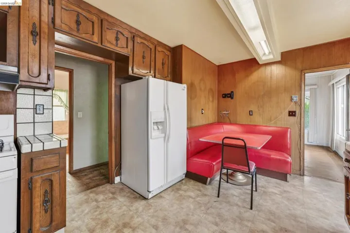 Kitchen featuring wood paneling, wood-finish cabinetry with decorative hardware, white tiled countertops, and a white refrigerator