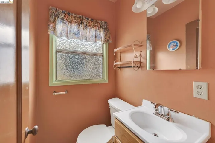 Bathroom featuring a single vanity with a white integrated sink, a mirrored medicine cabinet, a toilet, and a window with textured privacy glass
