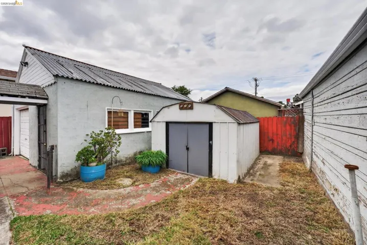 Rear exterior featuring a corrugated metal roof, stucco siding, and a detached storage shed