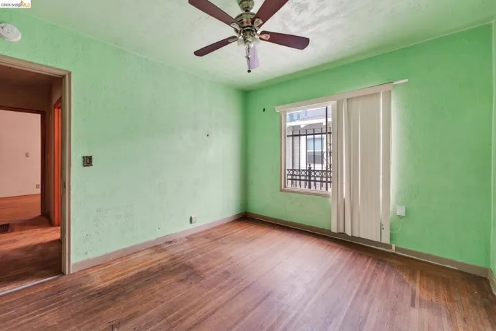 Room featuring wood-finish flooring, a ceiling fan with integrated lighting, and a window with security bars