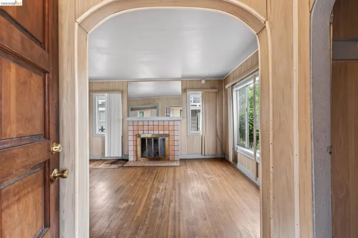 Arched entryway opening to a room featuring wood-finish flooring, a tile fireplace with a brass firebox, and multiple windows