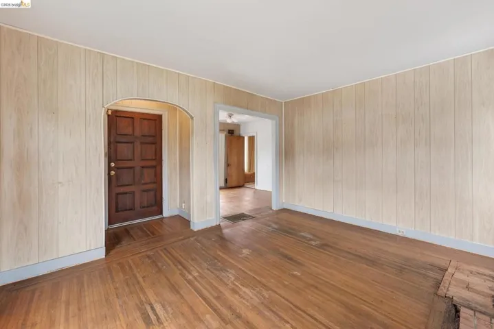 Interior space featuring wood-finish wall paneling, hardwood flooring, and a paneled entry door with an arched frame