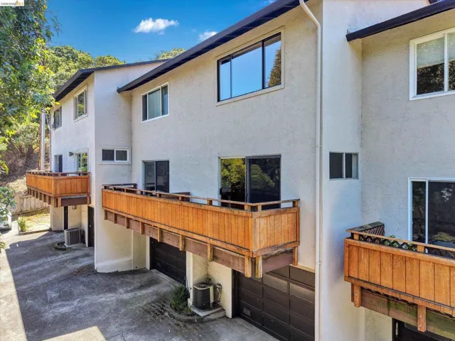 Multi-level stucco exterior featuring private balconies with natural wood railings, multiple windows, and integrated garage access