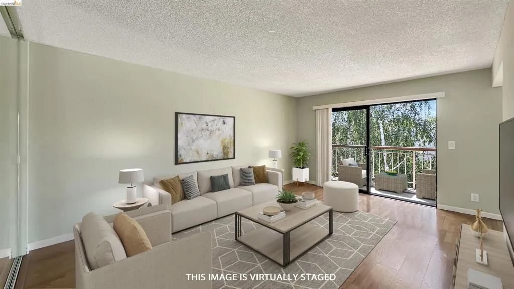 Spacious living area featuring wood-finish flooring, light-toned wall paint, and a sliding glass door leading to an outdoor balcony