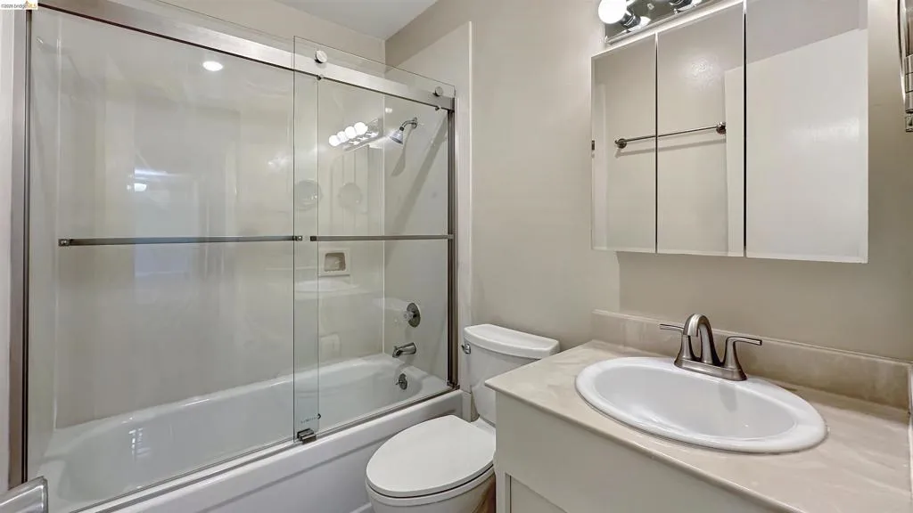 Bathroom featuring a combination tub and shower with glass sliding doors, a vanity with an integrated sink and light-toned countertop, and a mirrored medicine cabinet