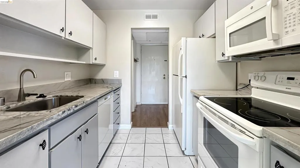 Galley kitchen with white cabinetry and patterned stone countertops