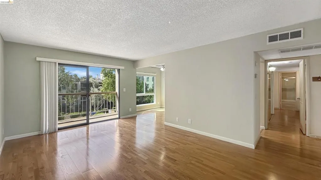 Bright interior space featuring wood-finish flooring, a sliding glass door to a private balcony, and multiple windows