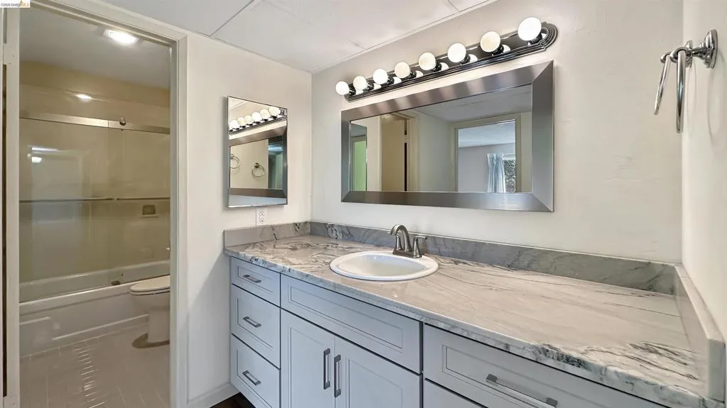 Bathroom vanity featuring a single basin sink, contemporary faucet, and a large framed mirror with overhead bar lighting