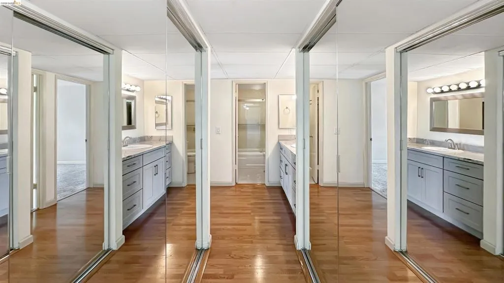Mirrored closet doors opening to a wood-finish flooring area with dual vanities