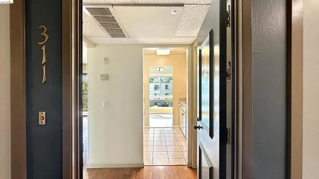 Wood-finish flooring extends from the entryway, leading towards a tiled kitchen area