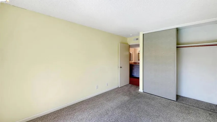 Carpeted room with light-toned walls, featuring a sliding door closet with one panel open to reveal a clothing rod