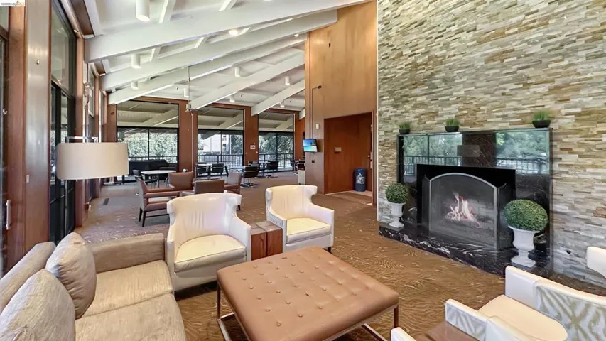 Spacious communal area featuring a stone accent wall, a built-in fireplace with a dark stone hearth, wood-paneled walls, and expansive windows