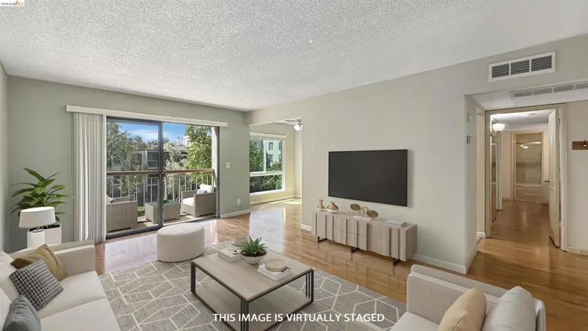 Living area featuring wood-finish flooring, a sliding glass door to a private balcony, and multiple windows