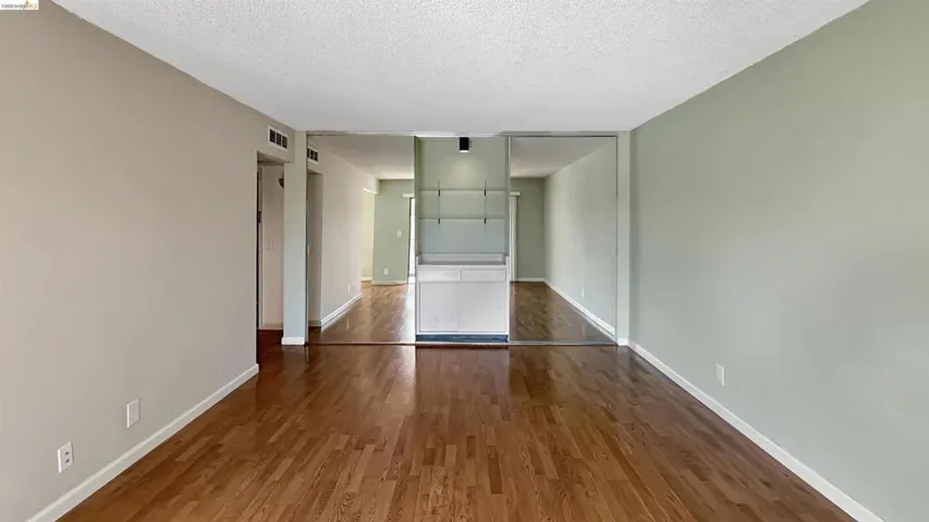 Interior room featuring wood-finish flooring, light green and beige wall finishes, and a built-in cabinet with open shelving and a mirrored wall