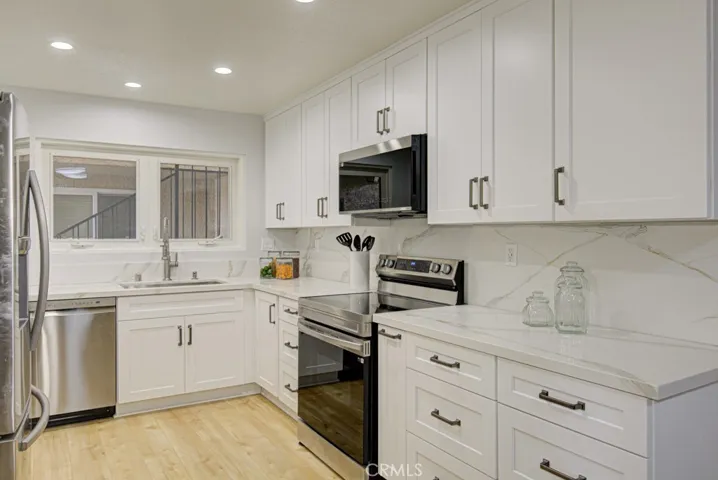 The kitchen has been updated with recessed lights,  white Shaker style cabinets and rich white quartz counters and backsplash.