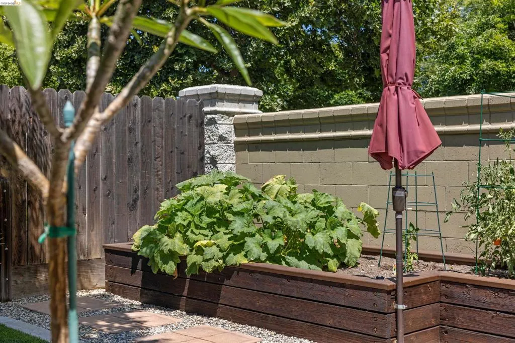Backyard featuring tiered wood-finish raised garden beds, a privacy fence, and a decorative block wall