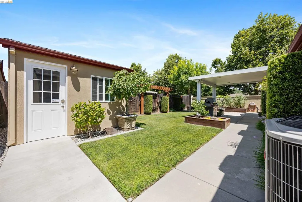 Expansive backyard featuring a manicured lawn, concrete pathways, and a covered patio structure
