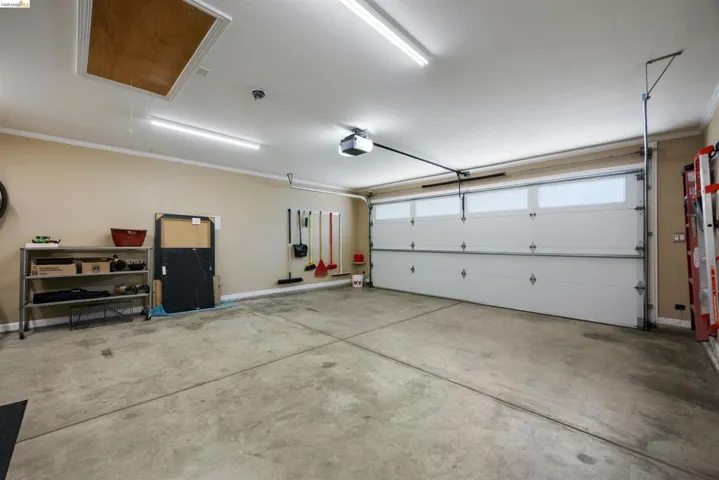 Spacious garage featuring a concrete floor, overhead lighting, an automatic garage door opener, and an attic access panel