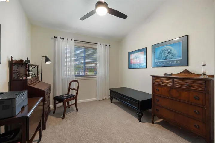 Room featuring neutral carpeting and walls, a vaulted ceiling, a window with blinds and sheer curtains, and a ceiling fan with integrated lighting