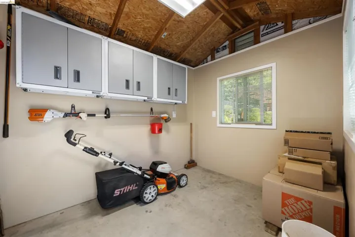 Utility shed featuring a concrete floor, painted walls, and an exposed wood beam ceiling
