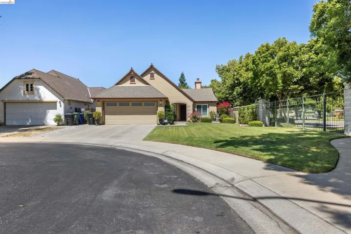 Stucco exterior residence featuring a two-car garage, pitched shingle roof, and a mature landscaped front lawn