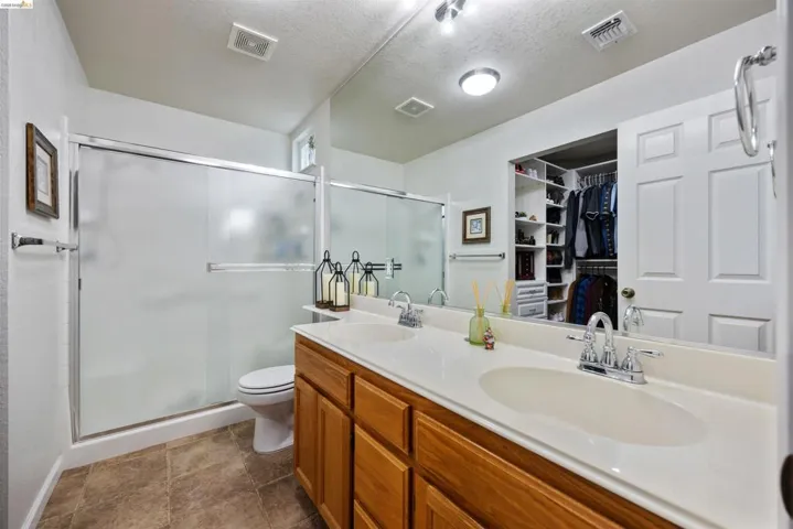 Bathroom vanity featuring dual sinks with chrome fixtures, wood-finish cabinetry, and a large wall-mounted mirror