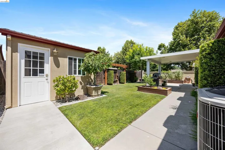 Expansive backyard featuring a manicured lawn, concrete pathways, and a covered patio structure