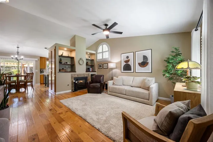 Open-concept living area featuring rich wood flooring, a fireplace with a stone surround, and built-in shelving
