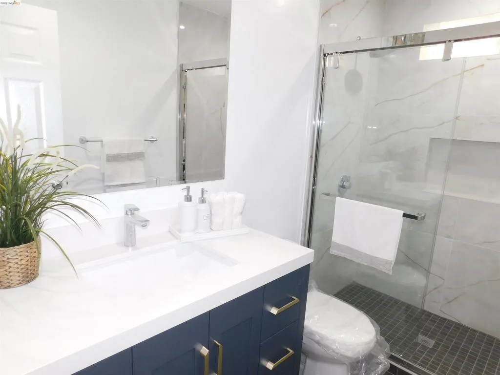 Bathroom featuring a navy blue vanity with gold-tone hardware, a white countertop with an integrated sink, and a frameless glass shower enclosure