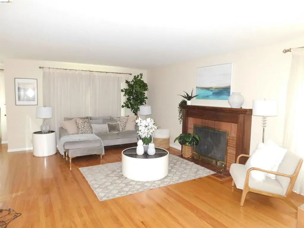 Living area featuring hardwood flooring, a fireplace with a brick surround and wood mantel, neutral wall tones, and sheer window treatments