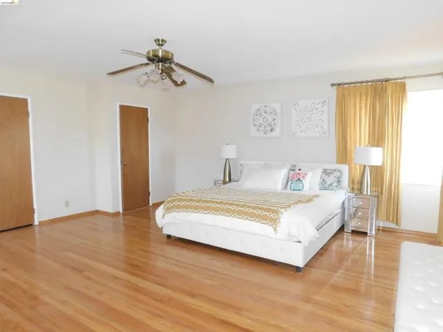 Bedroom featuring hardwood flooring, white walls, and a ceiling fan with integrated lighting