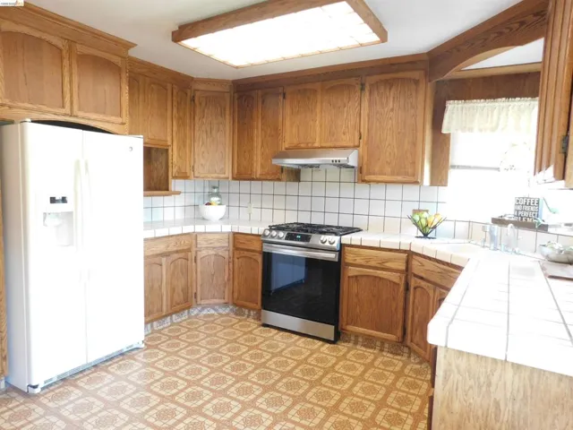 Kitchen featuring extensive wood cabinetry, white tile countertops, a white tile backsplash, stainless steel range with hood, and patterned flooring