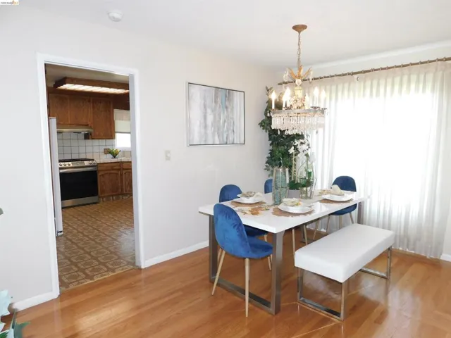 Dining area with wood-finish flooring, a decorative chandelier, and a large window with sheer drapes