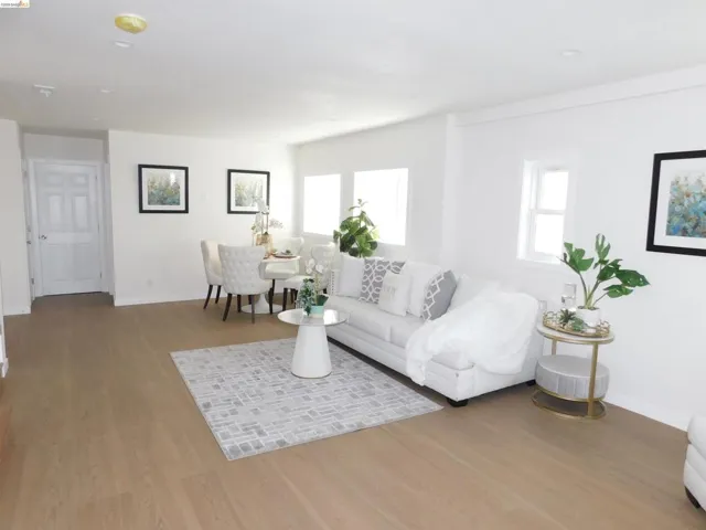 Open-concept living area featuring light wood-finish flooring, white walls, and multiple windows