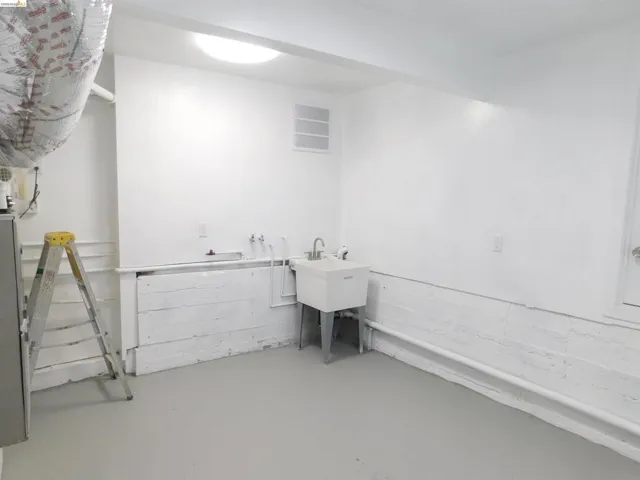 Utility room featuring a white basin sink with a chrome faucet, light gray flooring, white walls, and exposed utilities