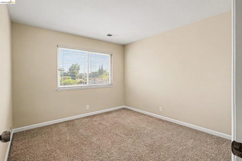 Interior room featuring neutral wall paint, textured carpet flooring, and a window with blinds