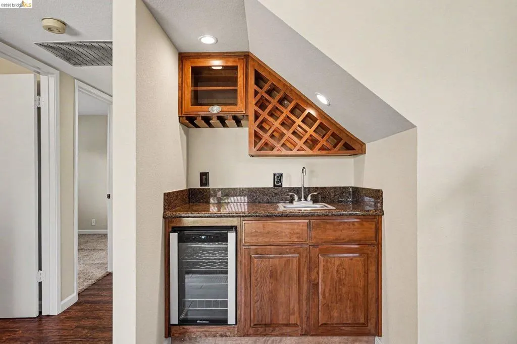 Built-in wet bar featuring wood cabinetry, granite-finish countertop, stainless steel sink, and an under-counter beverage cooler