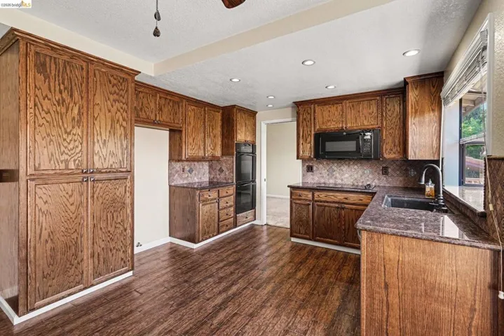 Kitchen featuring wood-finish flooring, recessed lighting, wood cabinetry, stone countertops, and a tile backsplash