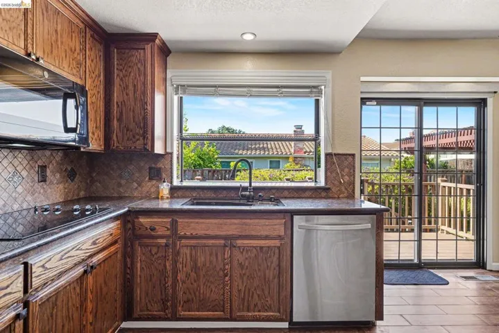 Kitchen featuring wood cabinetry, stainless steel dishwasher, integrated sink with dark faucet, built-in cooktop, and tile backsplash