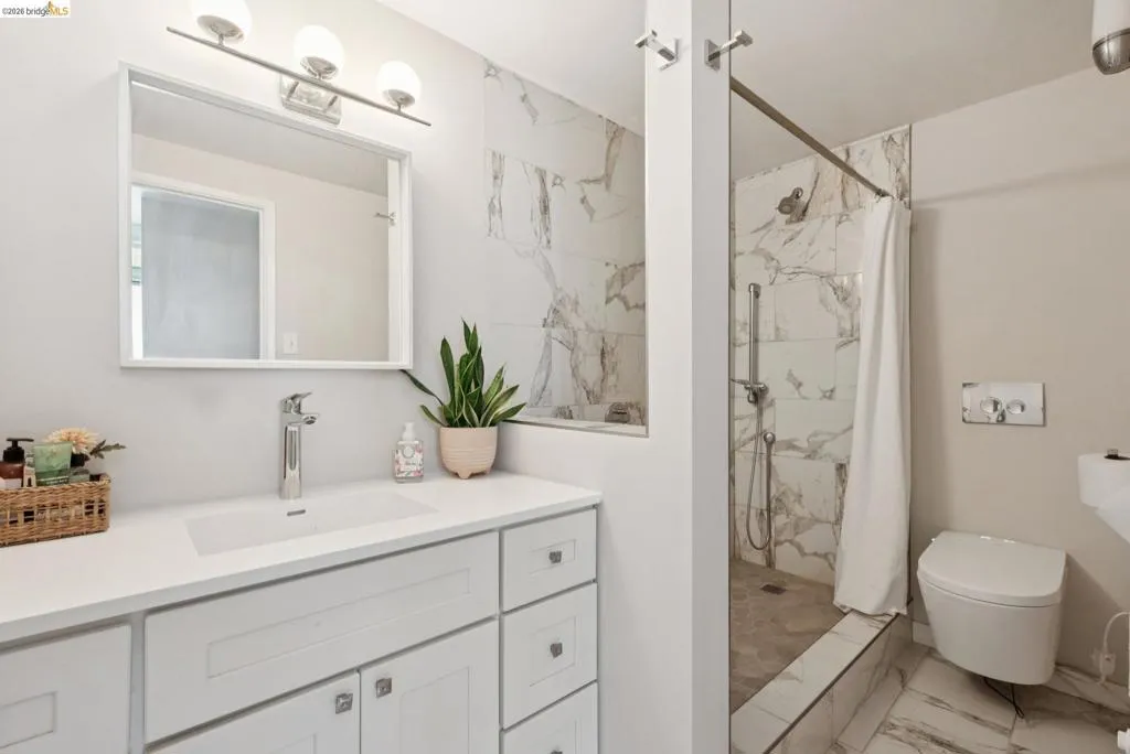 Full bath featuring vanity, a marble finish shower, and light marble finish floors
