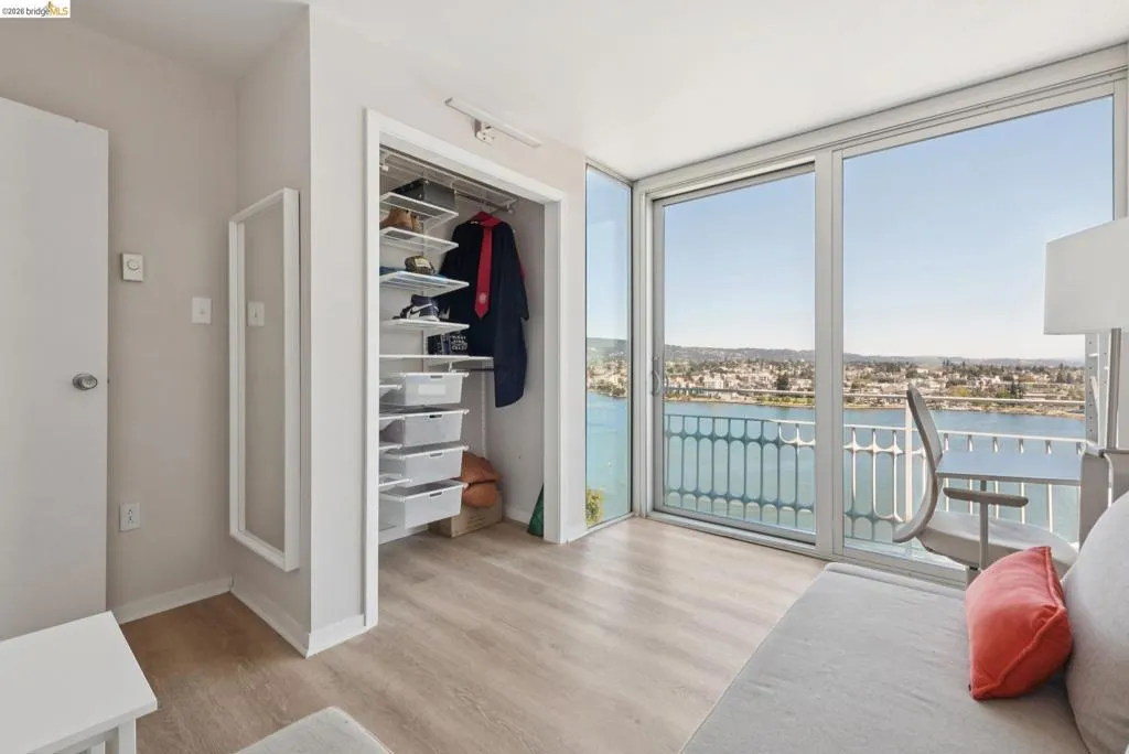 Bedroom with expansive windows, a water view, access to exterior, light wood finished floors, and a walk in closet