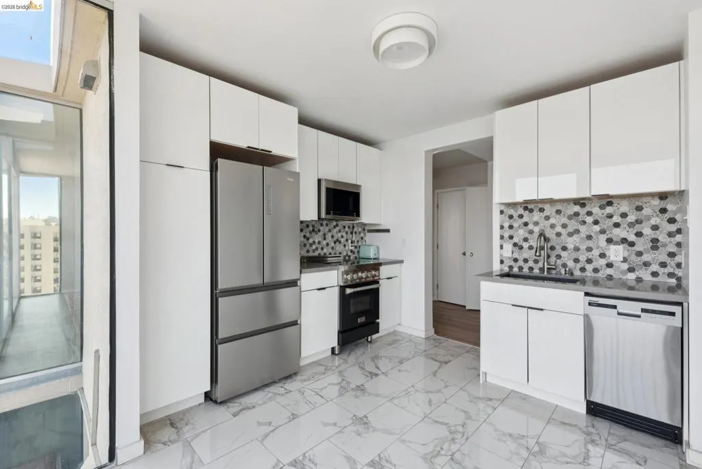 Kitchen featuring dark countertops, stainless steel appliances, tasteful backsplash, and white cabinets